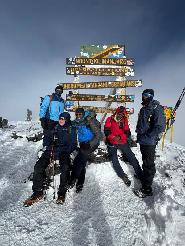 Uhuru Peak, 5,895 m, Africa's highest point. Nelson Mushi, seated in the blue jacket, with his team at the summit signboard after seven hours up from Barafu Camp.